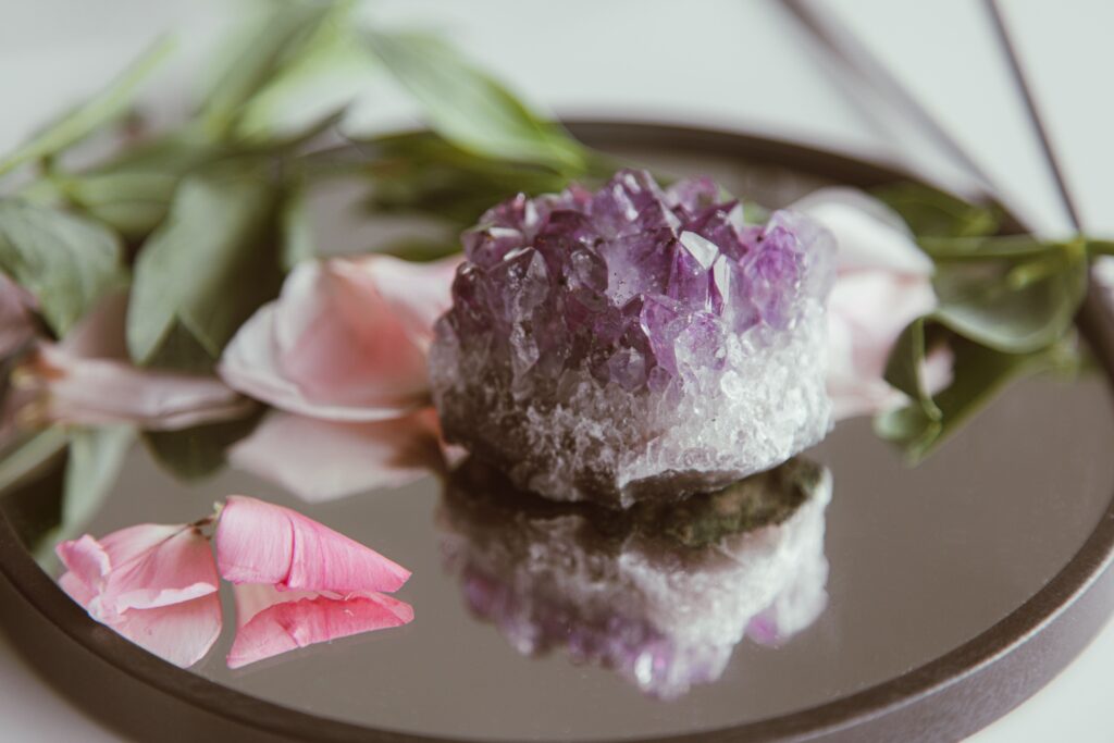 Elegant still life featuring amethyst crystal with pink flower petals on reflective surface.